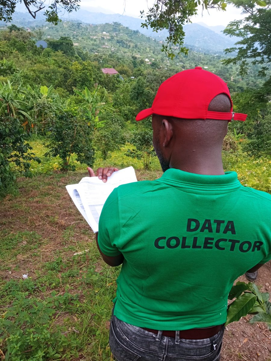 Impact Lines data collector with a survey form, looking over coffee and banana farms on a hillside